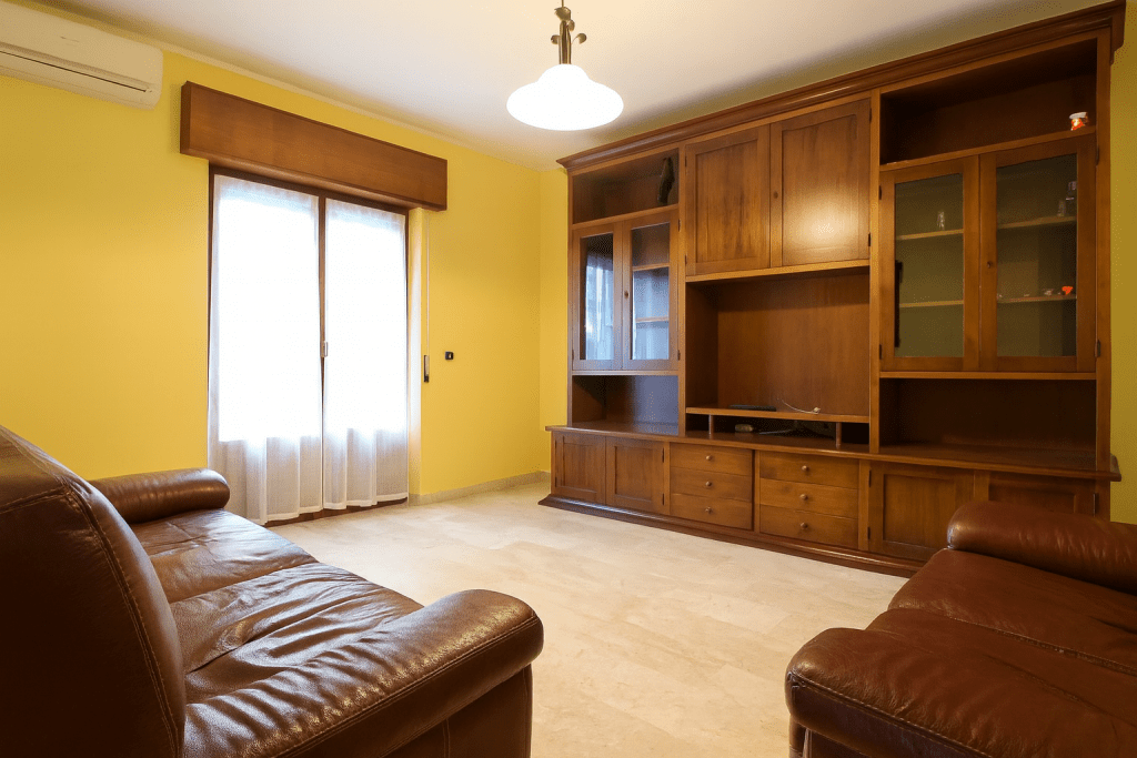 Soggiorno con libreria datata prima del virtual home staging avanzato.